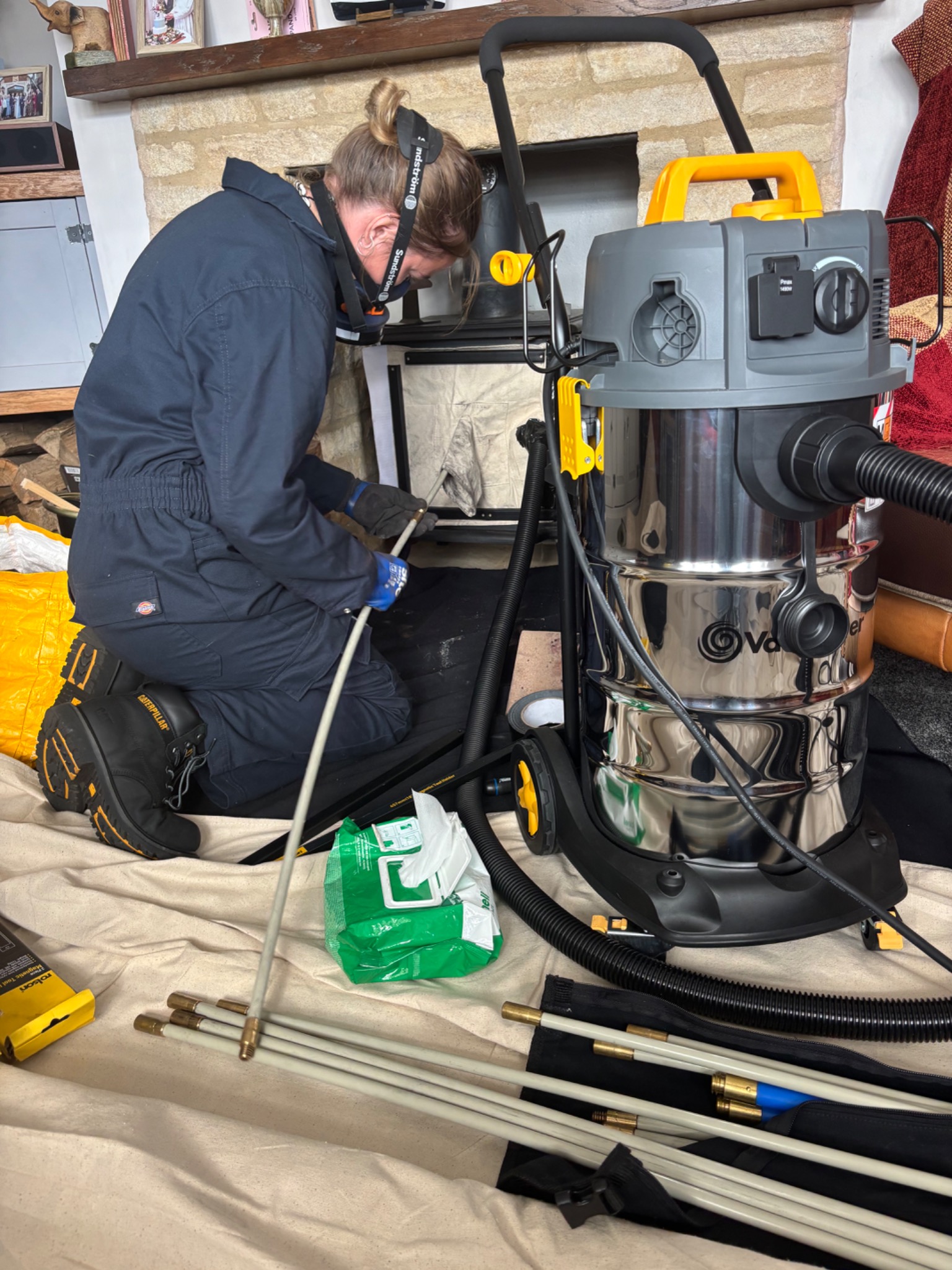 Megan working at a fireplace with a vacuum, chimney rods and protective floor sheets.