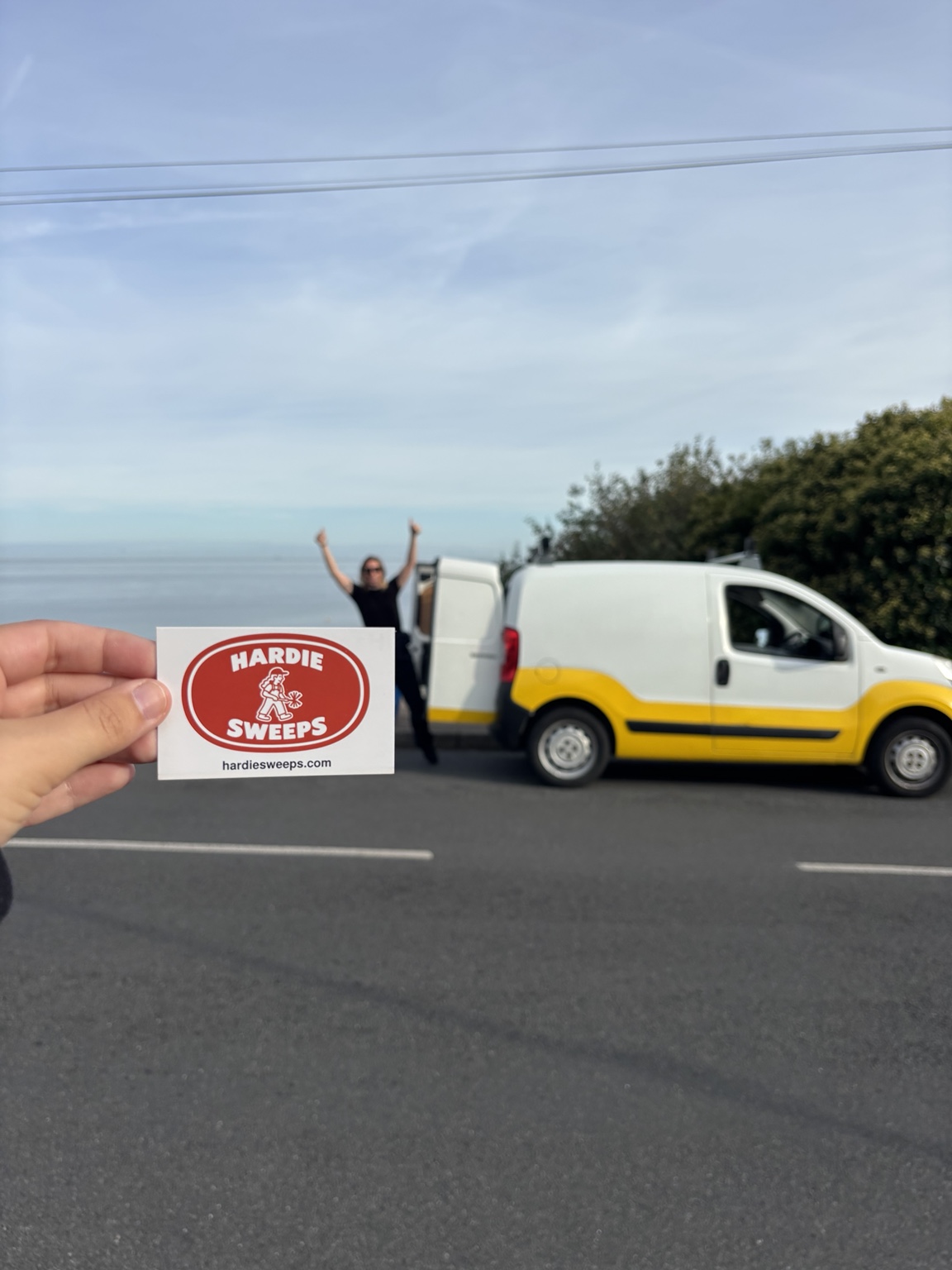 A Hardie Sweeps business card held in front of the yellow and white work van.