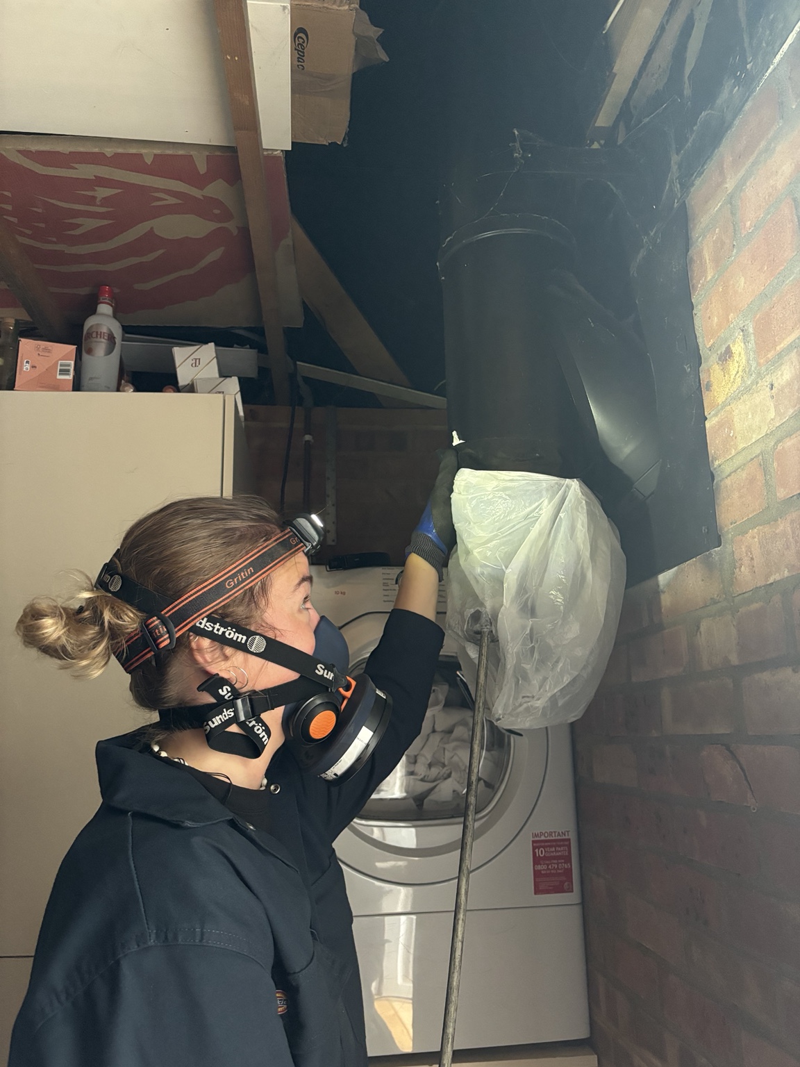 Megan wearing protective equipment while sweeping a flue beside a brick wall.
