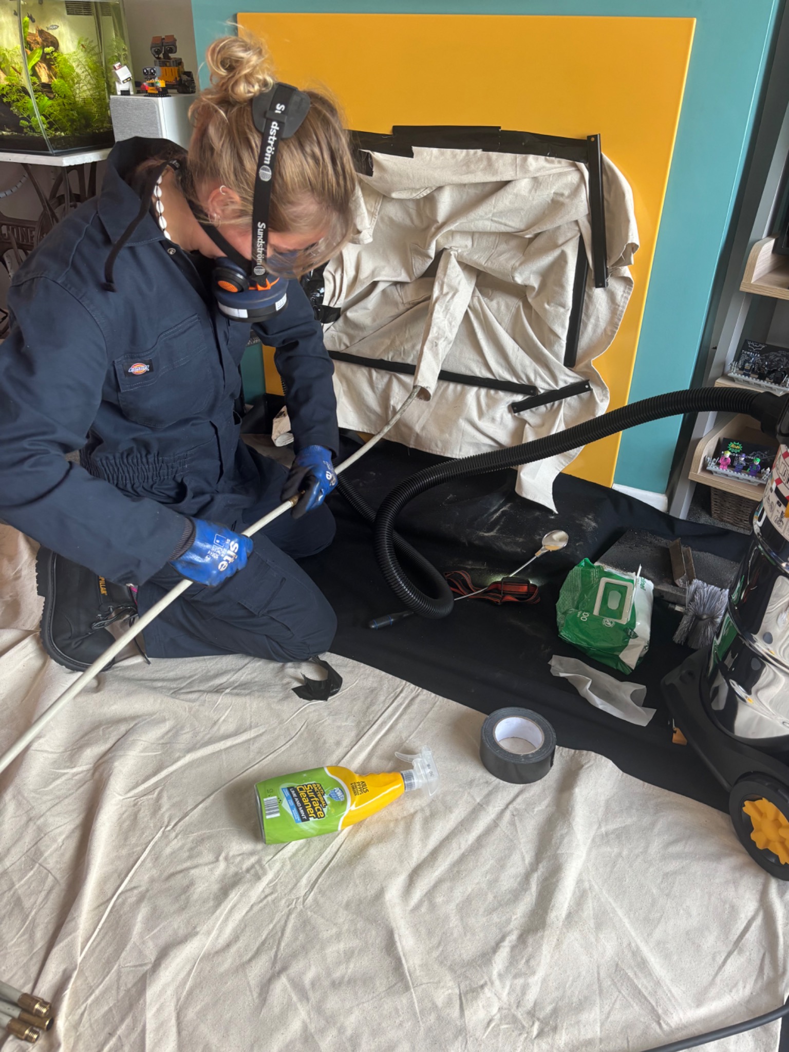 Megan sweeping a chimney with protective fireplace sheeting and a vacuum hose.