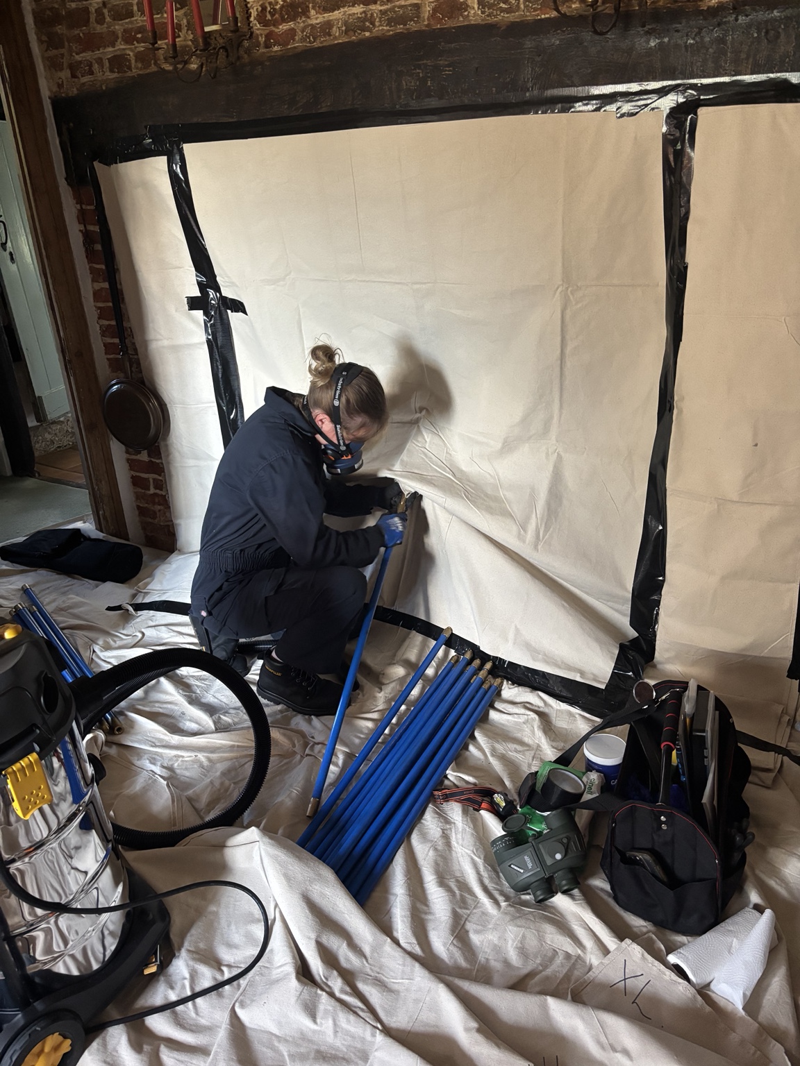 Megan sweeping a large inglenook with chimney rods and protective sheeting.