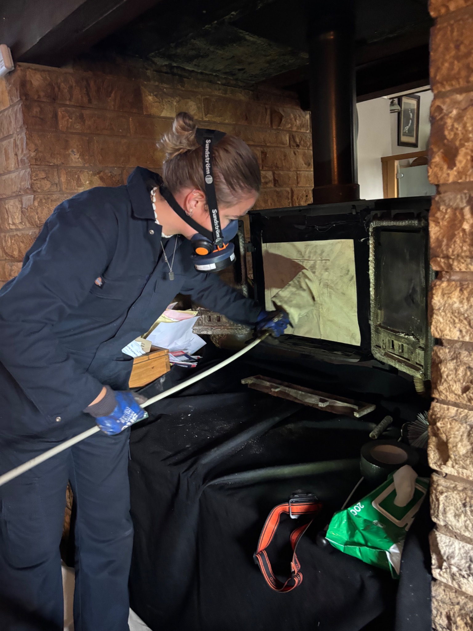 Megan wearing protective equipment and sweeping a log burner with chimney rods.