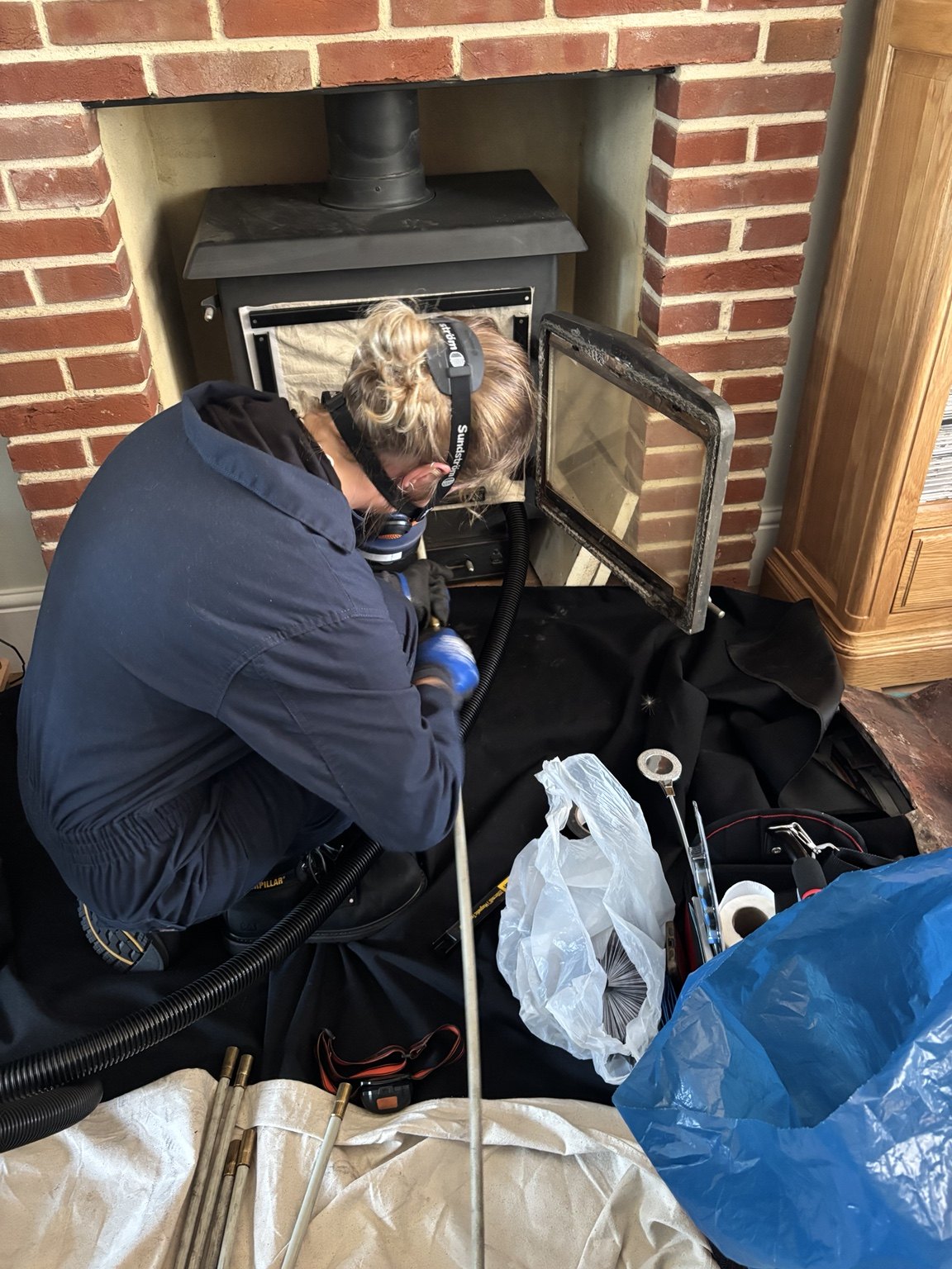 Megan sweeping a log burner in a brick fireplace with protective floor coverings.